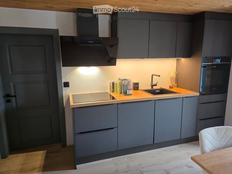 Modern kitchen with grey cabinets, wooden countertops, stainless steel appliances, and a built-in oven. Includes a sink, faucet, range hood, and various small items on the counter.