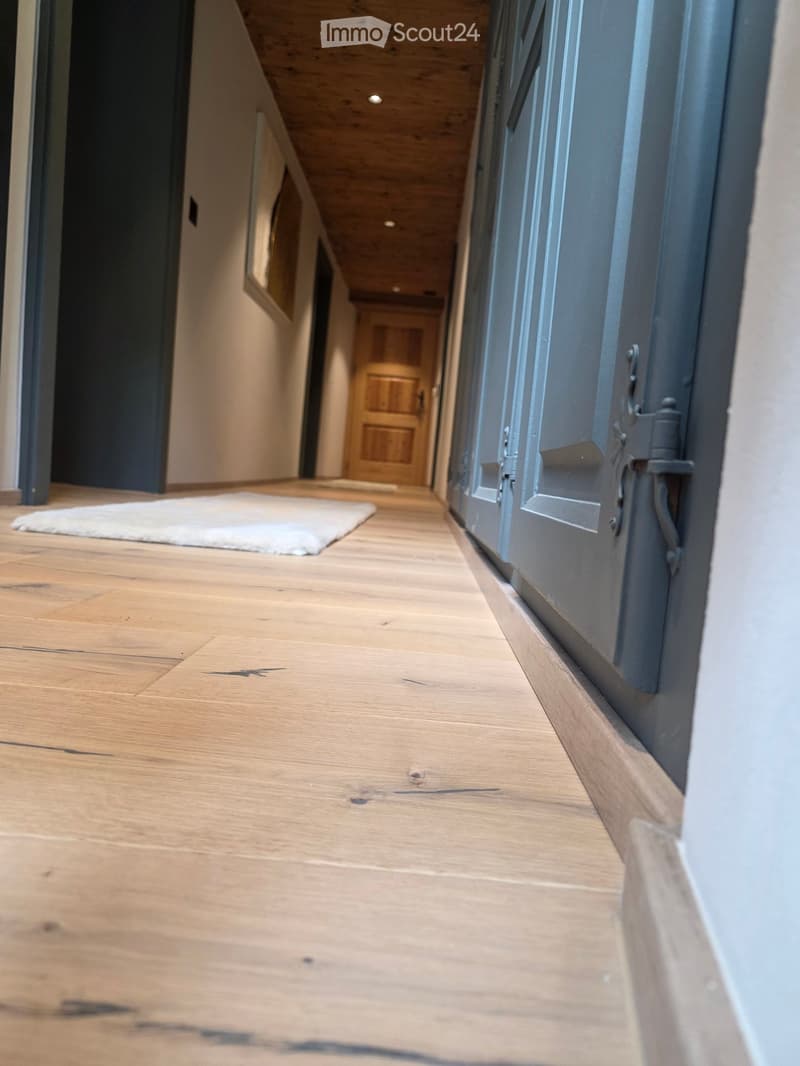 Wooden floor hallway with a white rug, wooden door, and recessed ceiling lighting.