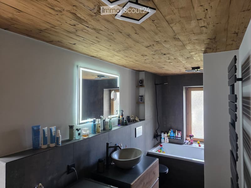 Modern bathroom with a wooden ceiling, large mirror, sink, bathtub, shelves, and various toiletries.