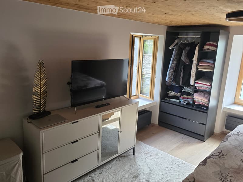 Modern bedroom with a large bed, wardrobe, TV on a stand, laptop, and decorative items.