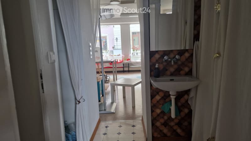 Hallway leading to a bathroom and a room with a table and chairs, featuring tiled floors and white walls.