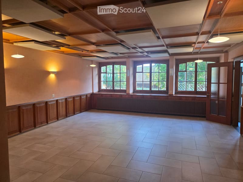 Empty room with wooden paneling, large windows, and a radiator. The space features a tiled floor and a wooden ceiling with recessed lighting.