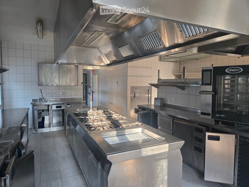 Commercial kitchen with stainless steel appliances, including a large stove, sink, refrigerator, microwave, and oven, all mounted on stainless steel countertops.