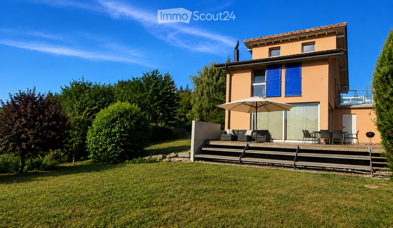 Two-story house with beige exterior, blue shutters, and a covered patio area with outdoor furniture and an umbrella.