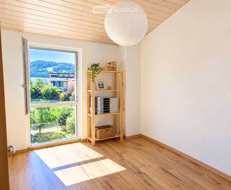 Bright, minimalist room with wooden flooring, large window offering scenic view, and a wooden shelf holding books, a picture frame, a plant, and a miniature house.