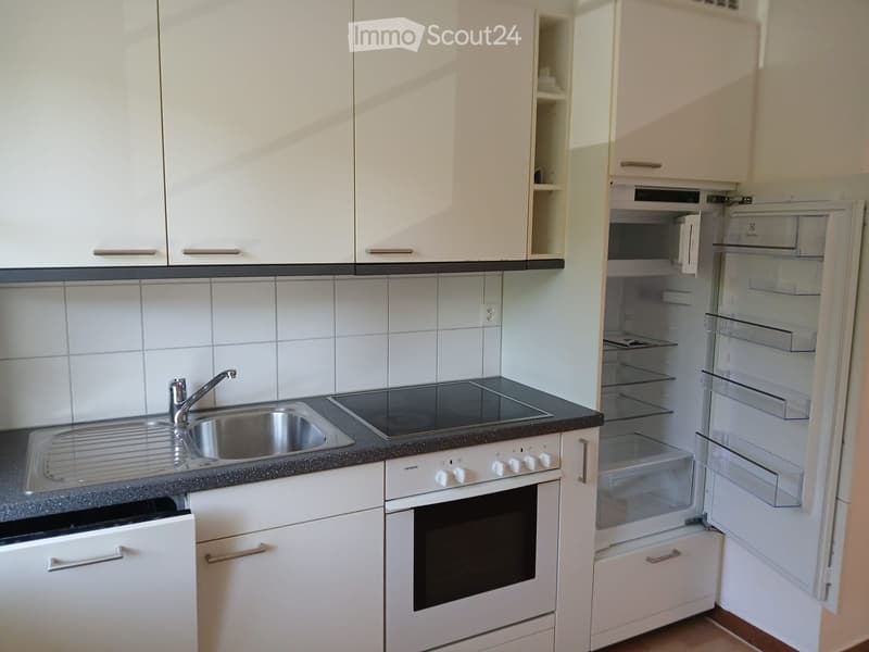 Modern kitchen with white cabinets, stainless steel sink, oven, and open refrigerator. Features tiled backsplash and granite countertop.