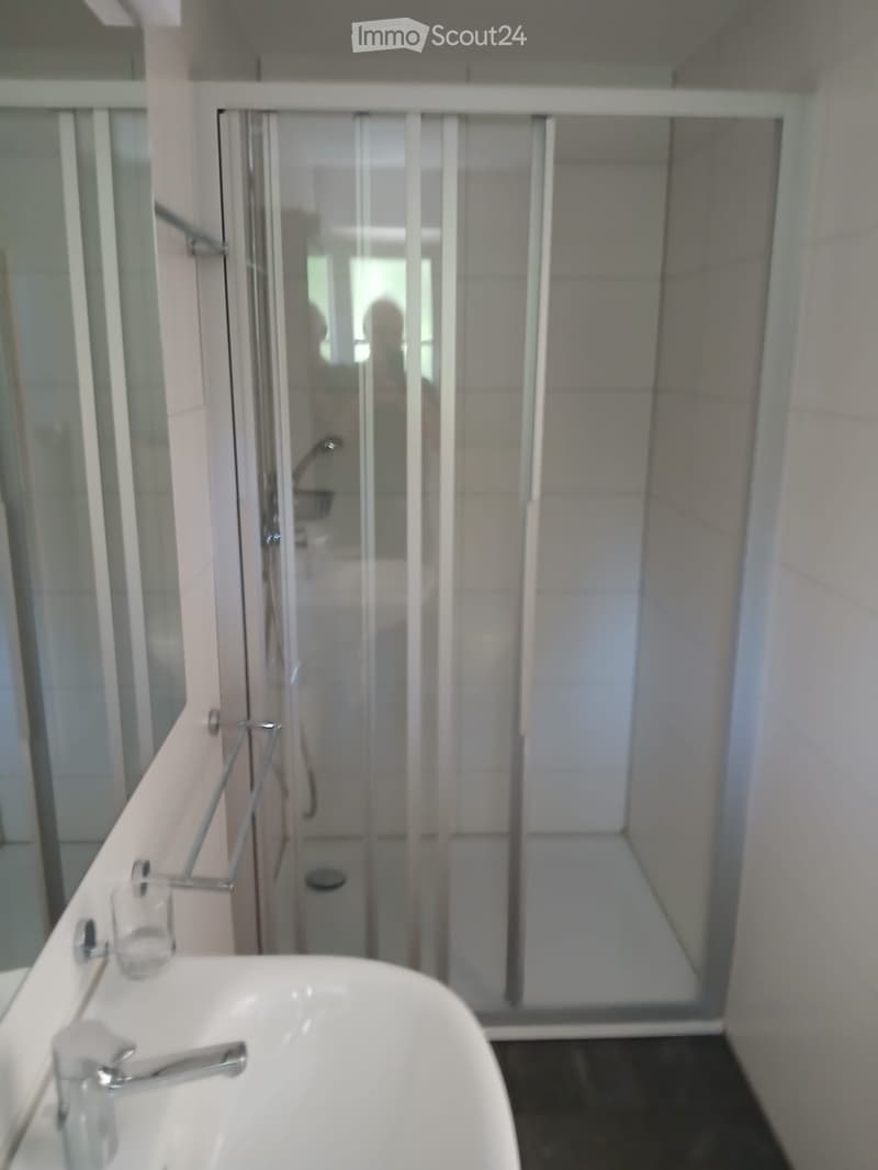 Modern bathroom with a white sink, faucet, cup, and a glass-enclosed shower stall.