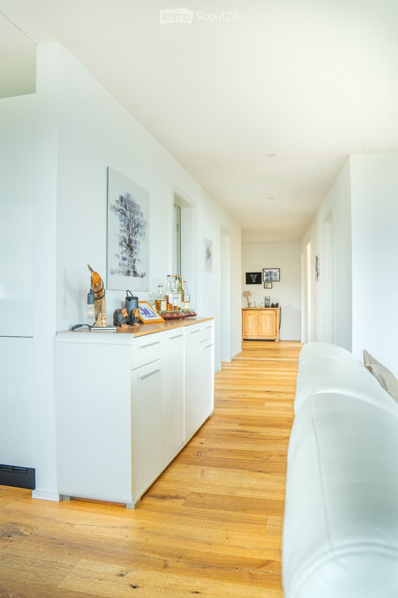 Bright hallway with wooden flooring, white walls, and modern decor including a small cabinet, artwork, and decorative items on a counter.