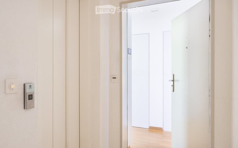 Opened door, wooden floor, elevator call panel, white walls