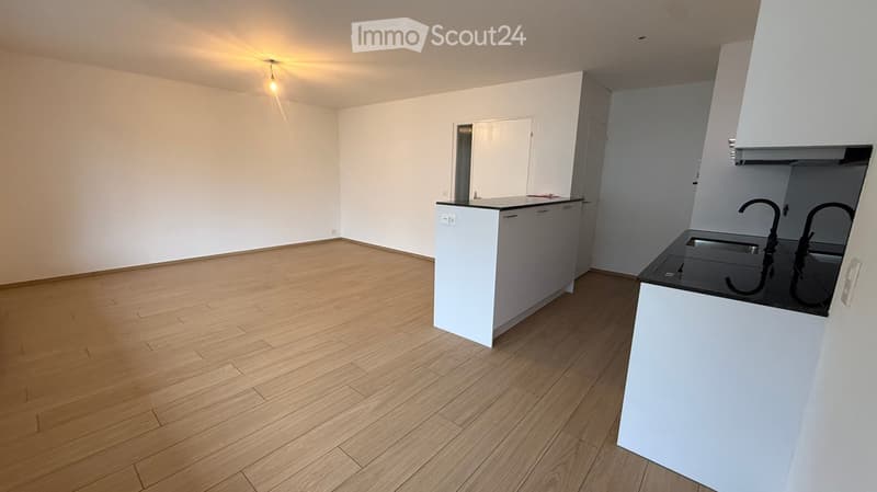 Modern kitchen with white cabinets, black countertop, and a sink with dual faucets. The floor is made of light wooden planks.