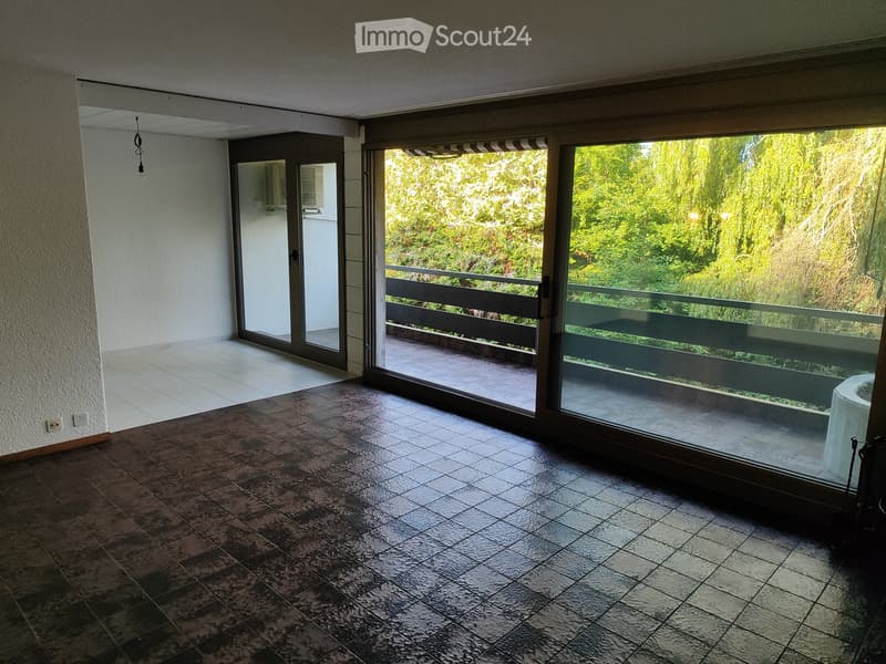 Empty room with tiled floor, large sliding glass doors leading to a balcony with a view of greenery.