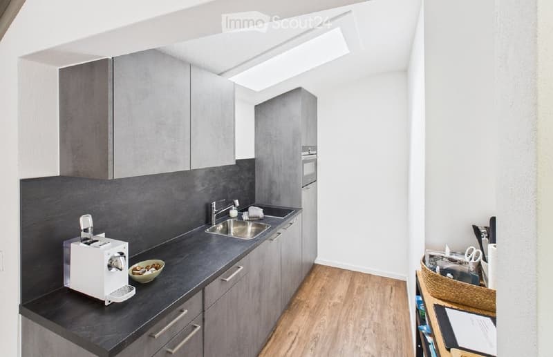 Modern kitchen with grey cabinets, dark countertops, a coffee maker, a sink, and a small basket on the floor.