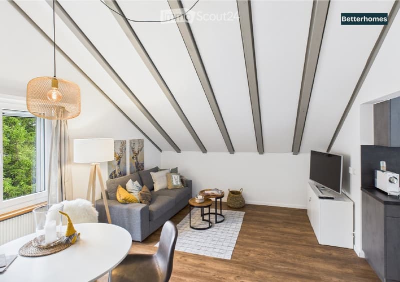 A modern, well-lit living room with a grey sofa, multiple side tables, a hanging lamp, a television, and a dining area with a white table and chairs. The room features wooden flooring and large windows with a view of greenery.