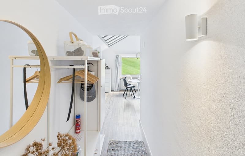 Modern hallway with white walls, wooden floor, built-in closet with hangers, round mirror, and a view into a dining area with chairs and table.