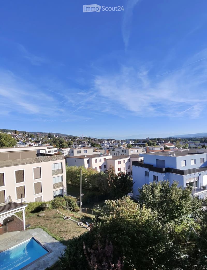 View of a residential area with multiple apartment buildings, trees, and a swimming pool in the foreground.