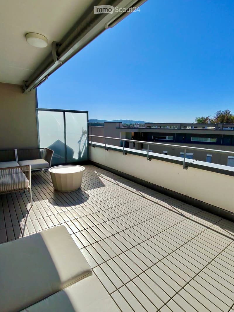 Balcony with wooden decking, white sofa, white chair, and a small round table.