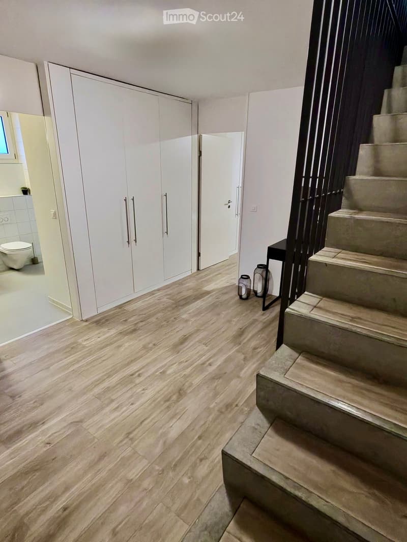Hallway with wooden flooring, white built-in closet, staircase leading upwards, and a small black table with decorative items.