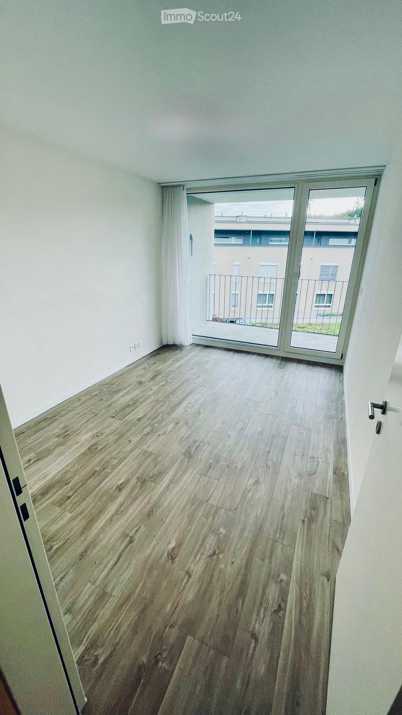 Empty room with light wooden flooring, white walls, and a large sliding glass door leading to a balcony area.