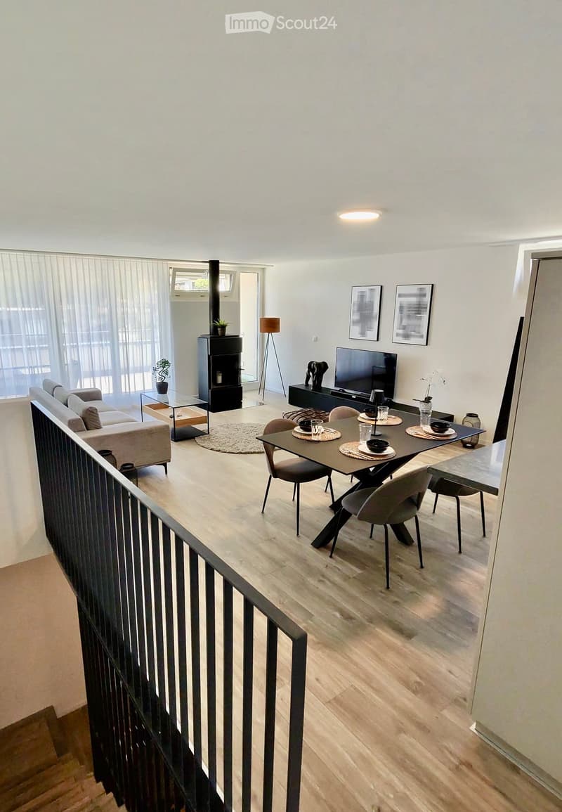 Modern living room with light wooden flooring, a grey sofa, a coffee table, a fireplace, a TV, a dining table with chairs, and a floor lamp.