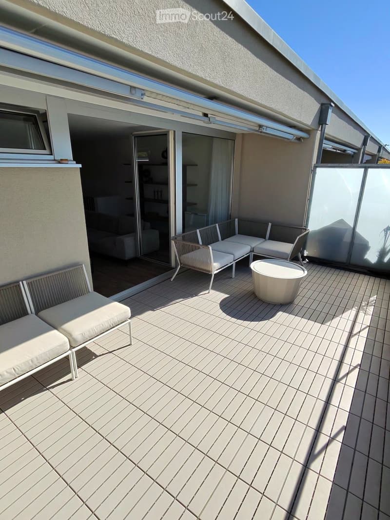 Balcony with tiled floor, white chairs, and a round table, connected to an indoor living space.
