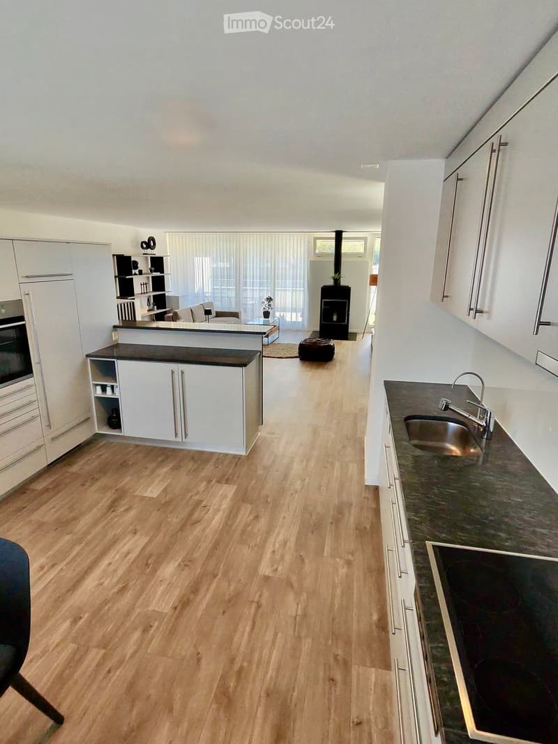 Open-plan kitchen and living area with light wooden flooring, white cabinets, a central island, a sink, and a fireplace.