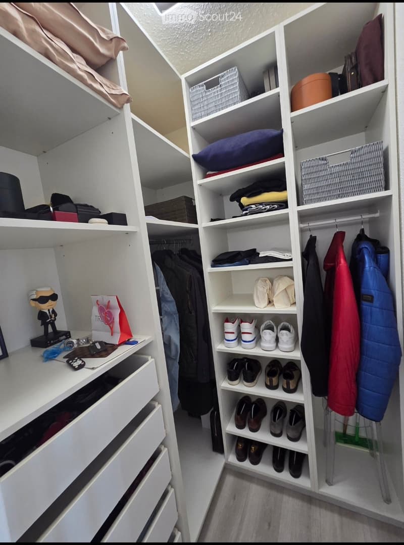 A well-organized walk-in closet with white built-in shelves and drawers, neatly arranged clothing, shoes, and accessories.