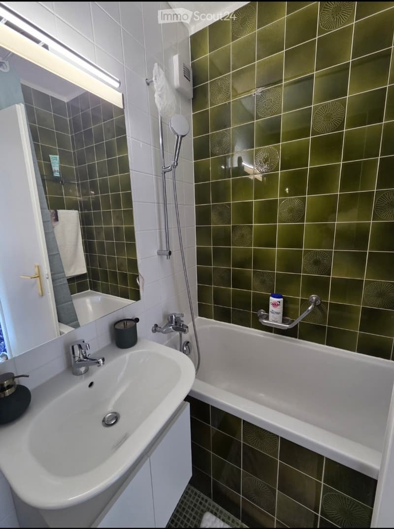 Modern bathroom with a white sink, bathtub, and showerhead. Green patterned tiles adorn the walls, and a towel hangs on the side.