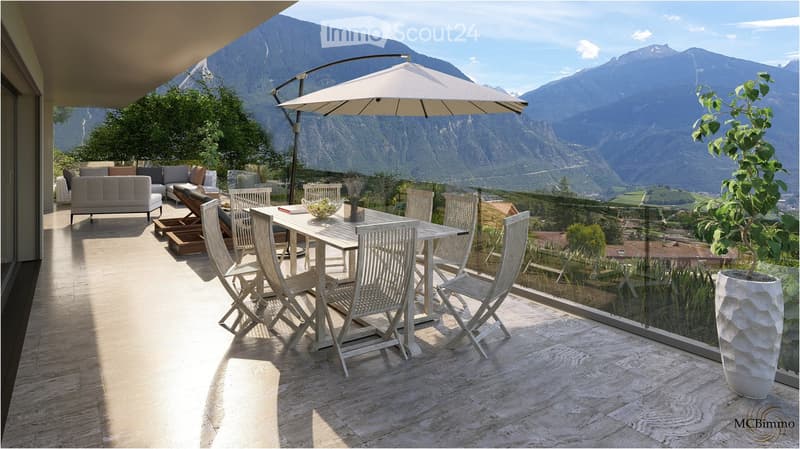 Balcony with a view of mountains, featuring a sofa, dining table with chairs, and an umbrella.