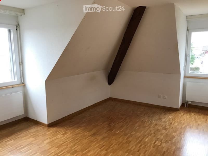 Empty room with wooden flooring, white walls, and large windows on two sides. No furniture or equipment present.