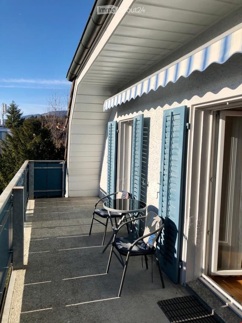 Balcony with a table and two chairs, featuring blue shutters and a striped awning.