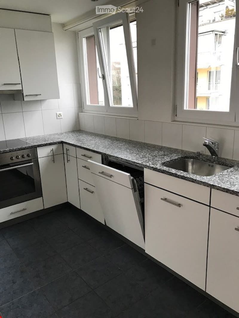 Modern kitchen with white cabinets, granite countertop, stainless steel sink and faucet, and built-in oven. Large windows provide natural light.
