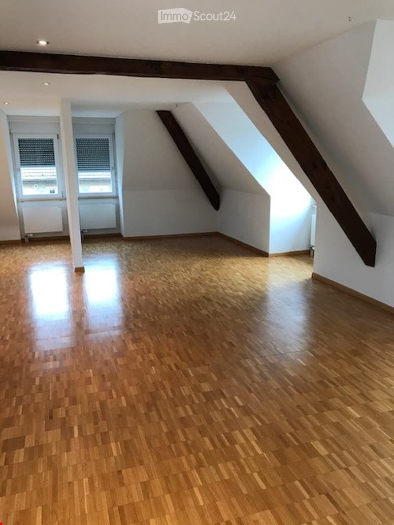 Empty attic room with wooden flooring, white walls, and exposed wooden beams. No furniture or equipment present.