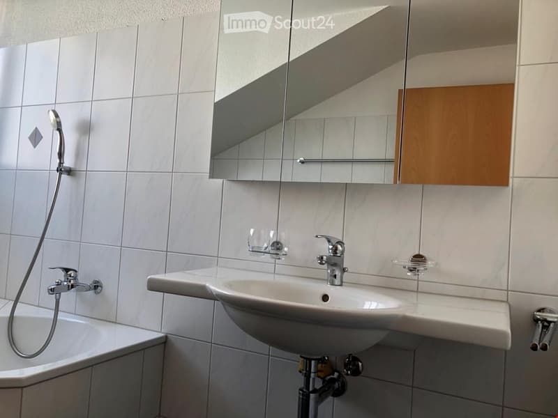 Modern bathroom with white tiled walls, a single sink with a chrome faucet, a large mirror with built-in storage, a bathtub, and a handheld showerhead.