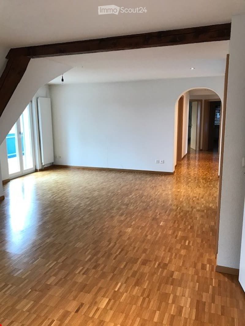 Completely empty room with wooden flooring, white walls, and large windows. No furniture or equipment.