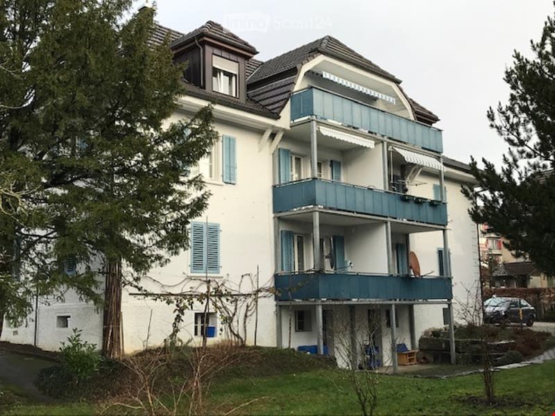 A multi-story residential building with light blue shutters, balconies, and a well-maintained lawn.
