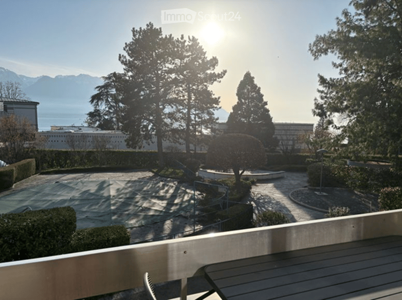 balcony with table, tennis court, hedges, trees, mountains, lake