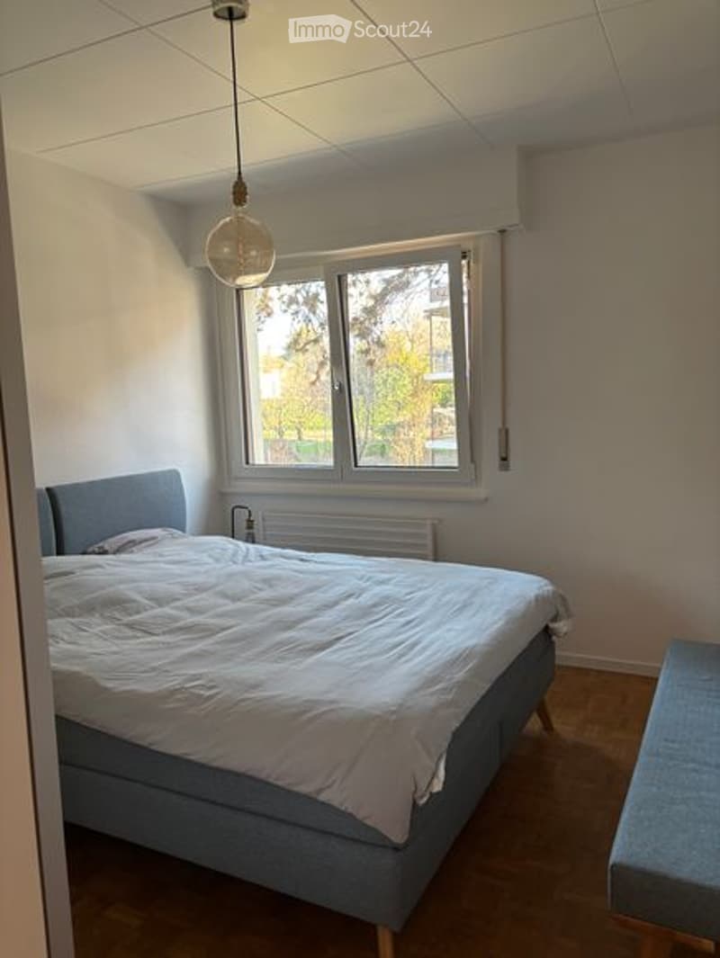 Bedroom with bed, window, radiator, wooden floor, bench, lamp