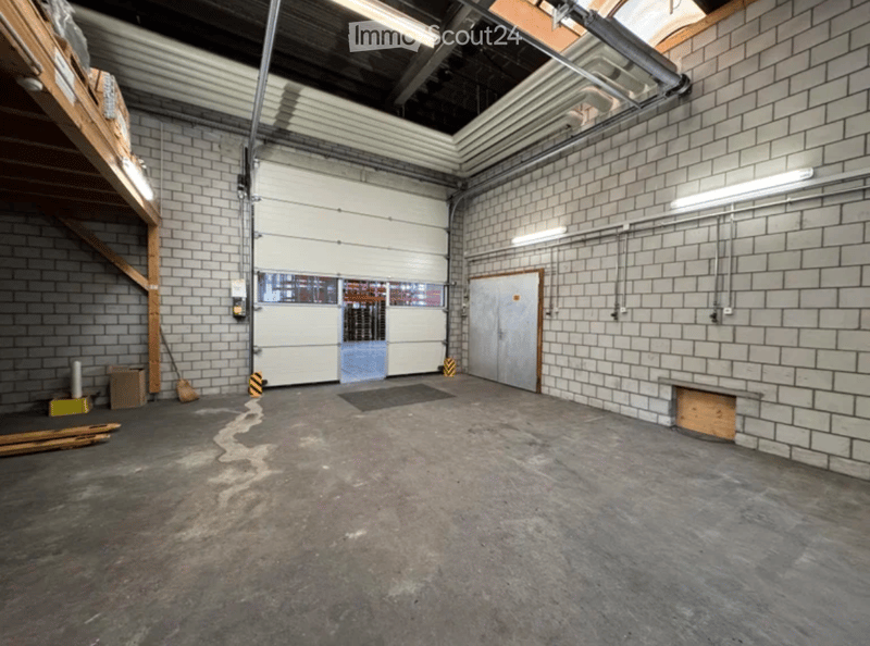 Empty industrial-style room with brick walls, concrete floor, large garage door, and minimal furnishings.