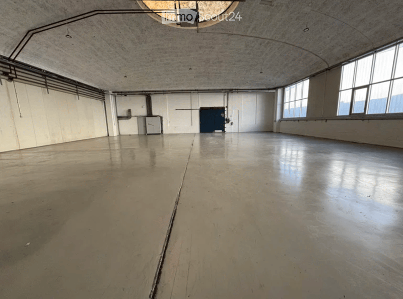 Empty industrial-style room with concrete floors, white walls, large windows, and minimal fixtures.