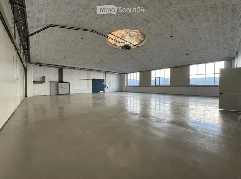 Empty industrial-style room with polished concrete floor, large windows, and a single hanging light fixture.