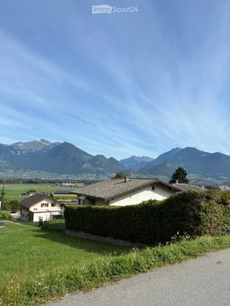 Single-family house with a pitched roof, surrounded by a well-maintained lawn and hedge, with a scenic mountain view in the background.