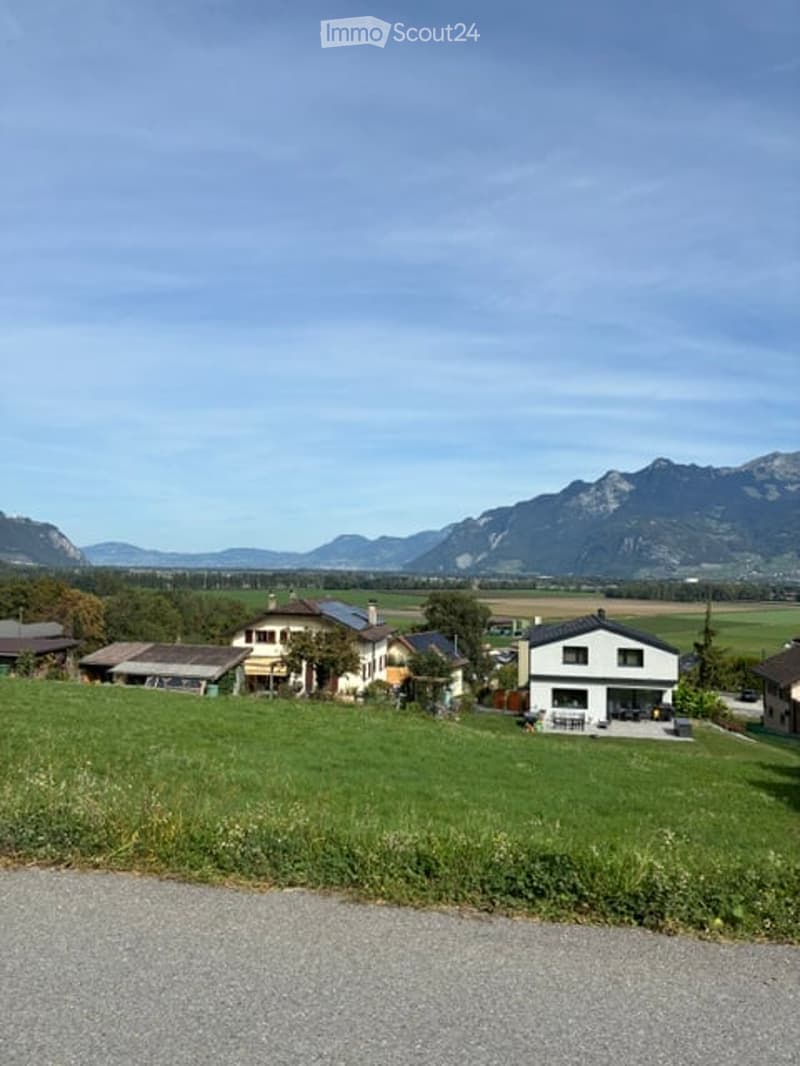 Scenic view of a rural house surrounded by green fields and mountains in the background.