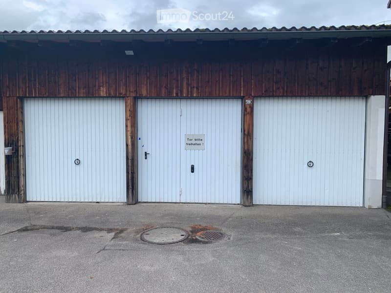 Three garage doors with a wooden facade and a sign in German reading "Tor bitte freihalten!" (Please keep the gate open!).