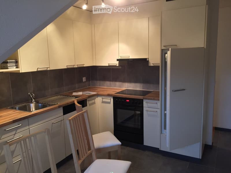 Modern kitchen with white cabinets, wooden countertops, stainless steel sink, oven, and two wooden chairs.