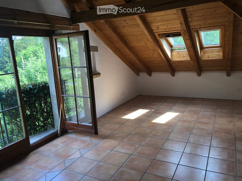 Empty attic room with wooden slanted ceilings, tiled floor, large windows, and a sliding glass door leading to the outside.