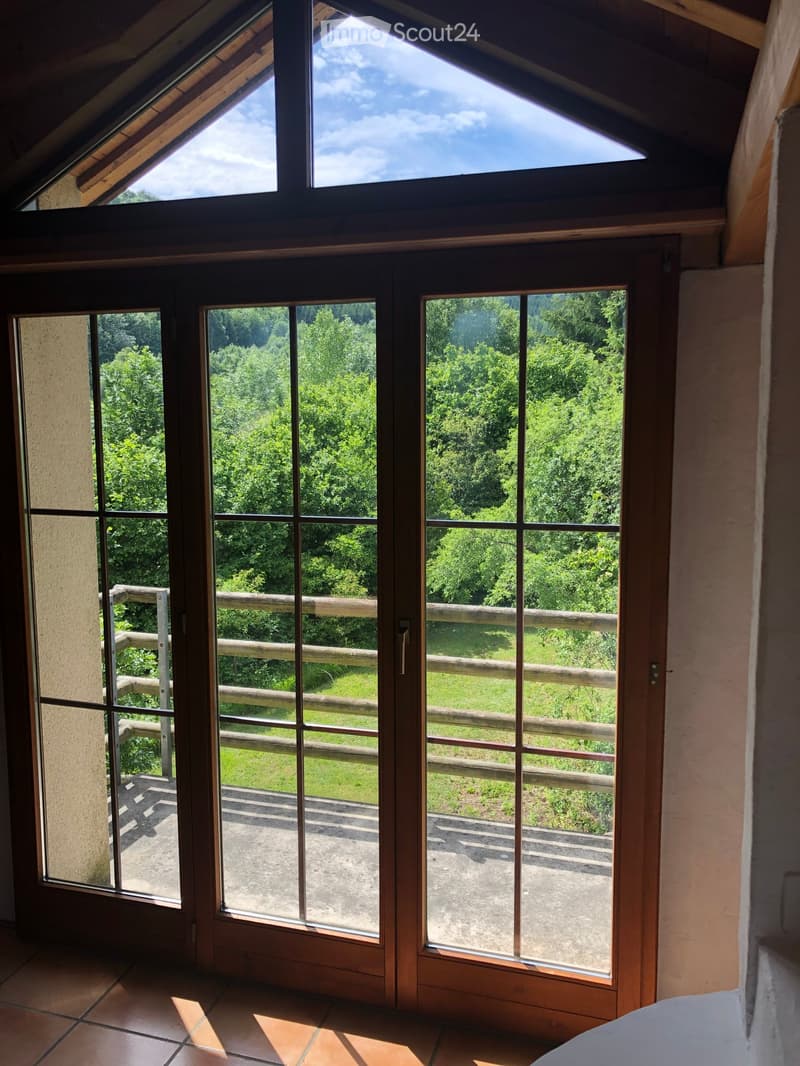 Bright room with large windows and sliding doors leading to a wooden deck with a scenic view of greenery and a grassy area.