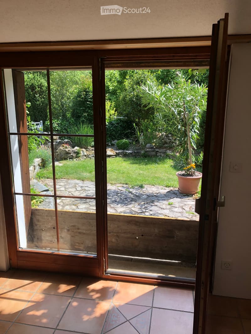 Open sliding glass door leading to a garden area with a stone pathway, potted plant, and lush greenery.