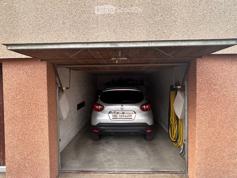 Garage with a silver car parked inside, featuring a wooden ceiling and textured walls.