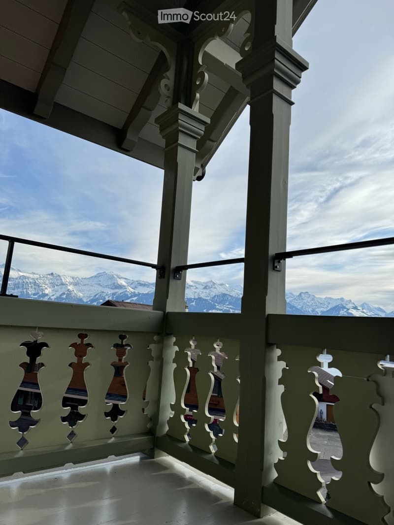 Balcony with ornate wooden railings and a scenic mountain view in the background.