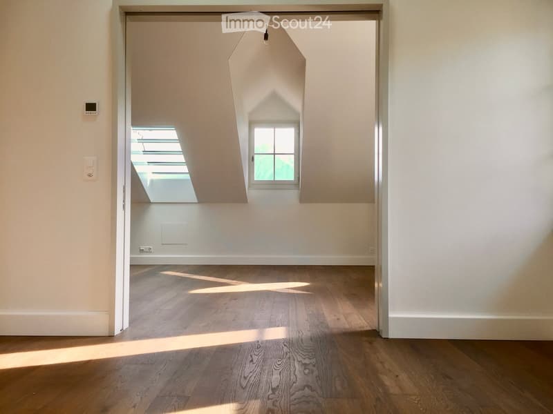 Empty room with wooden flooring and white walls, featuring a skylight and a window, illuminated by natural light.